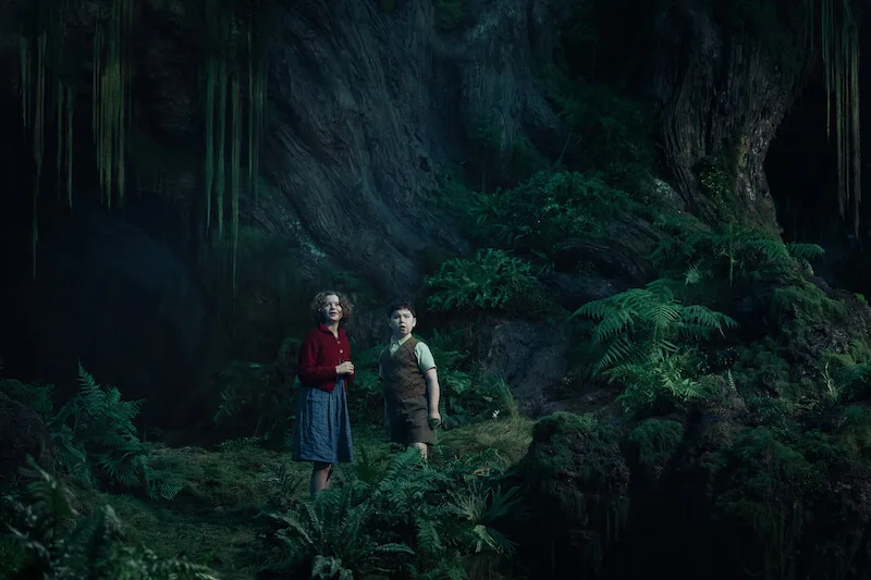 Digory et Polly dans une forêt luxuriante, image officielle de Narnia : Le Neveu du magicien
